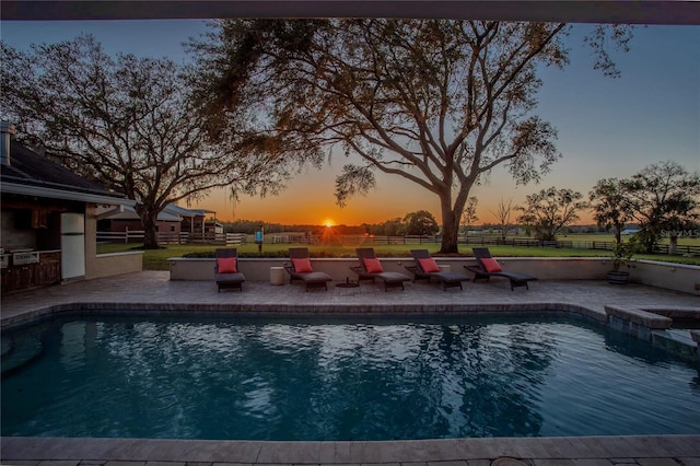 pool at dusk featuring an outdoor pool, a patio, and fence