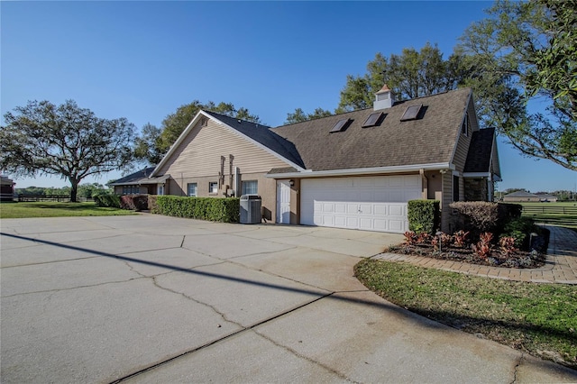 view of property exterior with a shingled roof, central air condition unit, concrete driveway, a chimney, and an attached garage