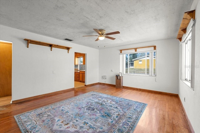 empty room featuring baseboards, visible vents, light wood-style flooring, and a textured ceiling