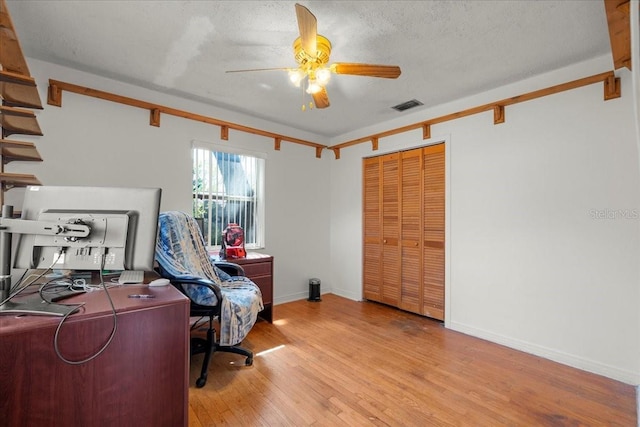 home office featuring a textured ceiling, a ceiling fan, baseboards, visible vents, and light wood-style floors