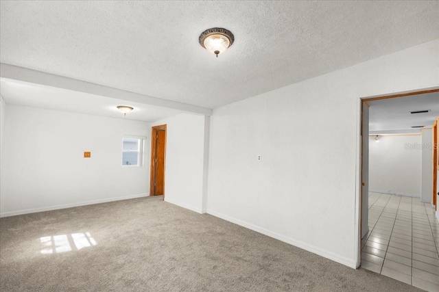 empty room featuring a textured ceiling, tile patterned flooring, carpet flooring, and baseboards