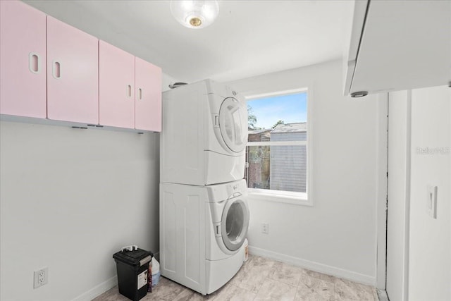 laundry room featuring stacked washer and dryer, cabinet space, and baseboards