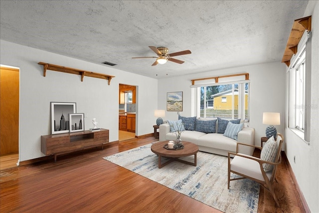 living room with a textured ceiling, wood finished floors, visible vents, and baseboards