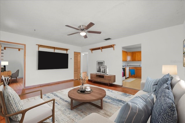 living room with light wood-style floors, ceiling fan, visible vents, and baseboards