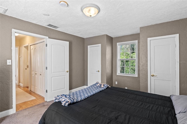 carpeted bedroom featuring baseboards, visible vents, a textured ceiling, and a textured wall