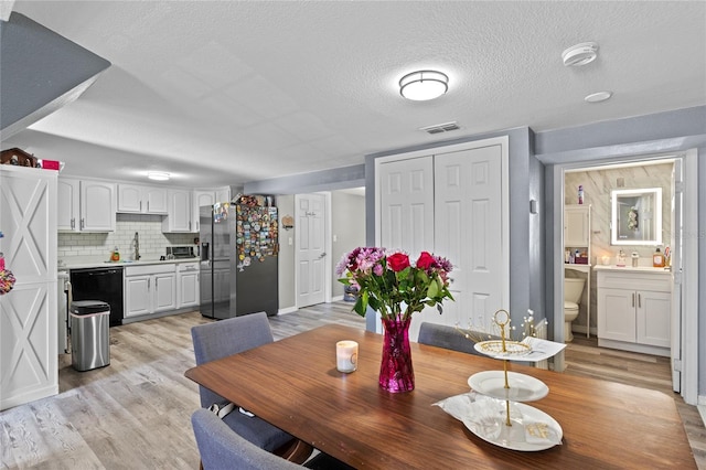 dining area featuring a textured ceiling, light wood-type flooring, and visible vents