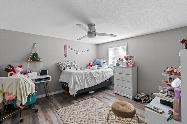 bedroom with a ceiling fan, a textured ceiling, baseboards, and wood finished floors