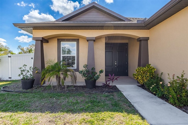 property entrance featuring a lawn, fence, and stucco siding