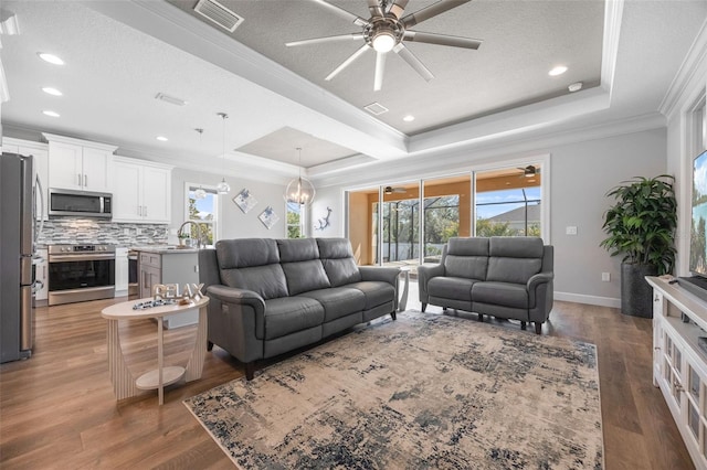 living room with a tray ceiling, plenty of natural light, visible vents, and crown molding