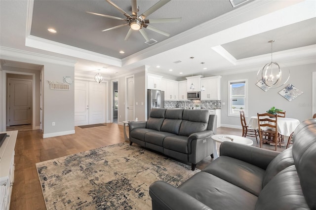 living room with baseboards, visible vents, wood finished floors, a tray ceiling, and crown molding