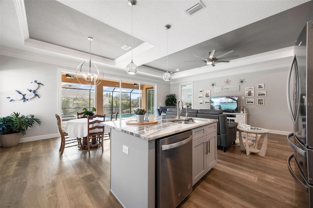 kitchen with light stone counters, stainless steel appliances, a sink, visible vents, and a tray ceiling