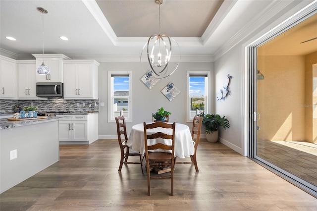 dining room featuring crown molding, wood finished floors, a raised ceiling, and a notable chandelier