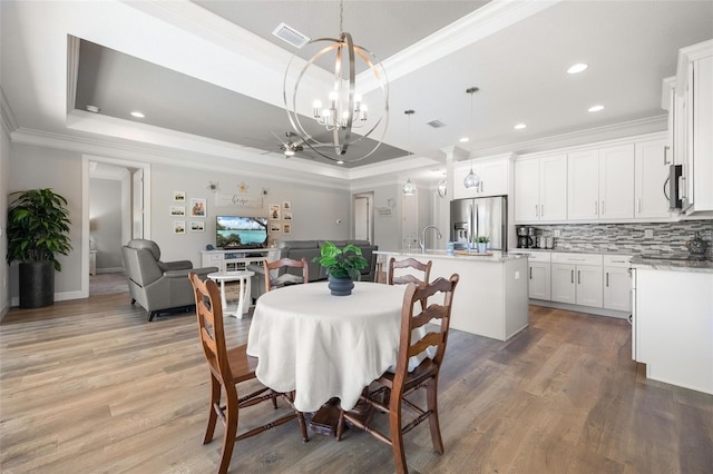 dining space with a tray ceiling, visible vents, an inviting chandelier, ornamental molding, and light wood-type flooring