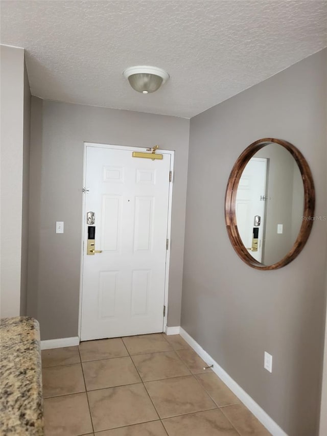 foyer featuring light tile patterned floors, baseboards, and a textured ceiling