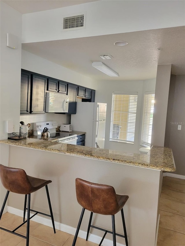 kitchen featuring visible vents, white appliances, a peninsula, and a kitchen bar