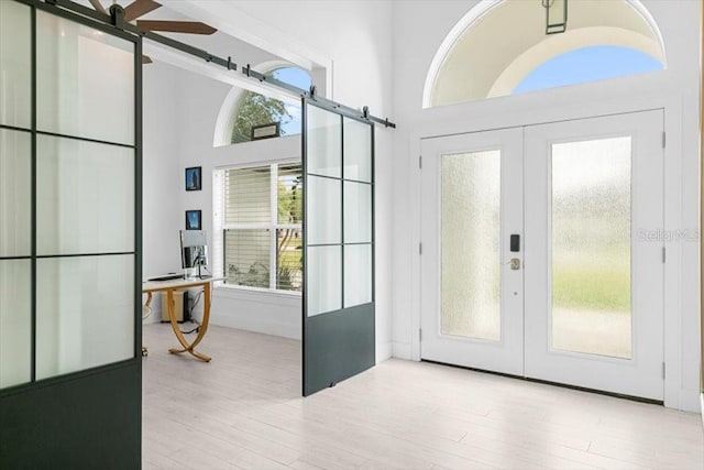 entryway with a healthy amount of sunlight, a towering ceiling, wood finished floors, and french doors