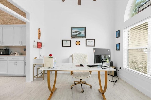 office space featuring light wood-style floors, ceiling fan, a towering ceiling, and baseboards