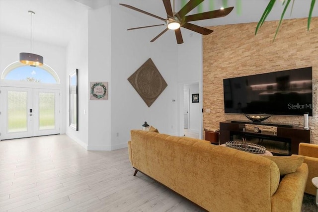 living area with ceiling fan, a towering ceiling, baseboards, light wood-style floors, and french doors