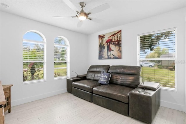 living area featuring light wood-type flooring, a ceiling fan, and baseboards