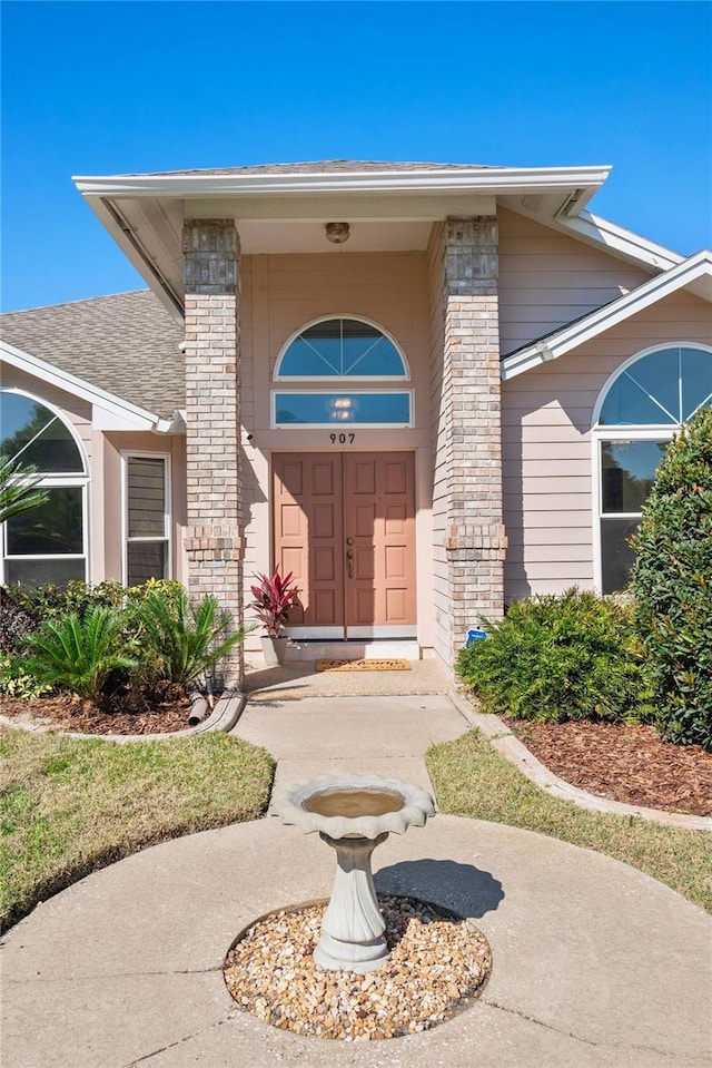 view of exterior entry featuring brick siding and roof with shingles