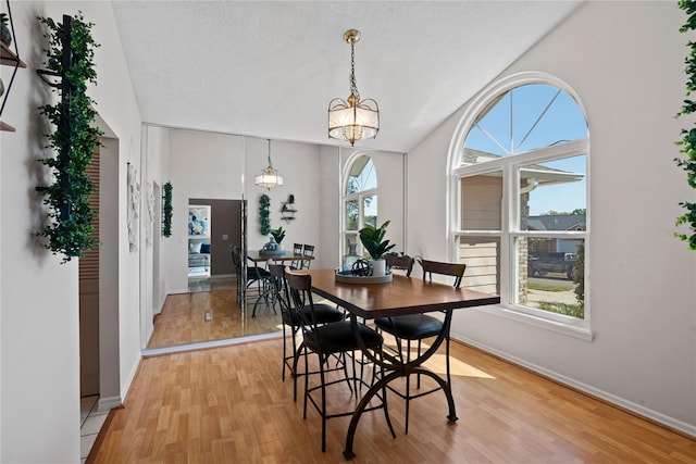 dining room with light wood finished floors, a notable chandelier, a textured ceiling, and baseboards