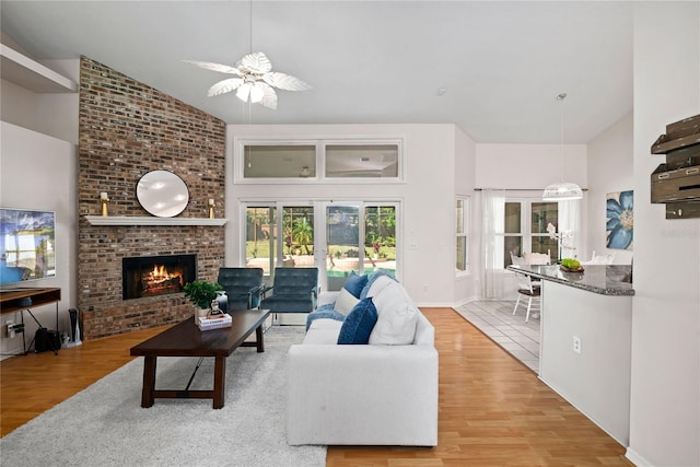 living room featuring a fireplace, wood finished floors, a ceiling fan, and high vaulted ceiling