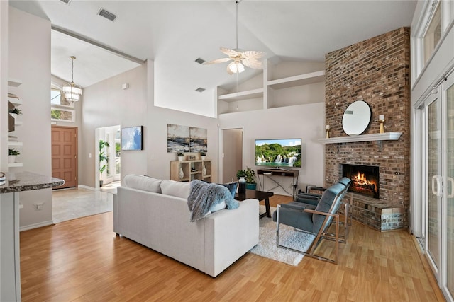 living area with ceiling fan with notable chandelier, a fireplace, high vaulted ceiling, and light wood-type flooring