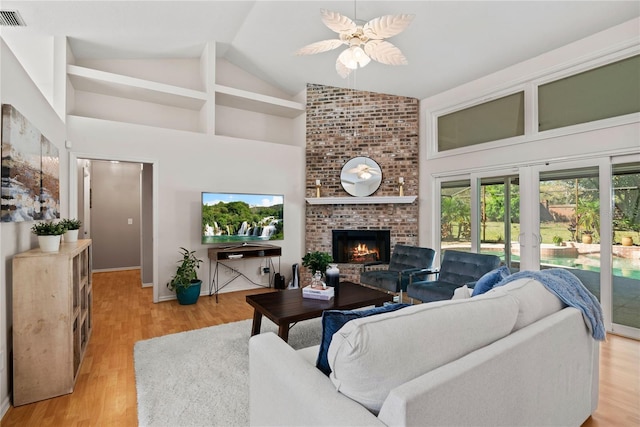 living area with visible vents, a brick fireplace, ceiling fan, light wood-style flooring, and high vaulted ceiling