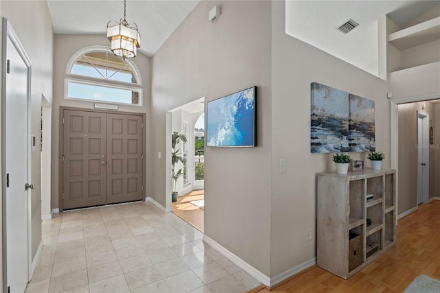 entryway with visible vents, baseboards, a chandelier, light tile patterned floors, and a towering ceiling