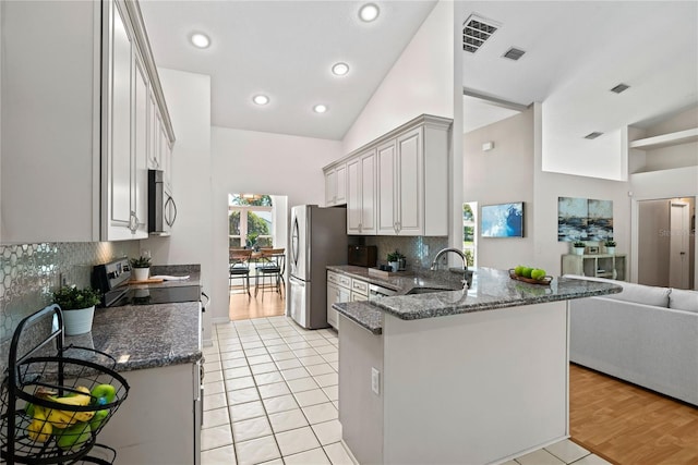 kitchen featuring open floor plan, dark stone countertops, appliances with stainless steel finishes, a peninsula, and a sink