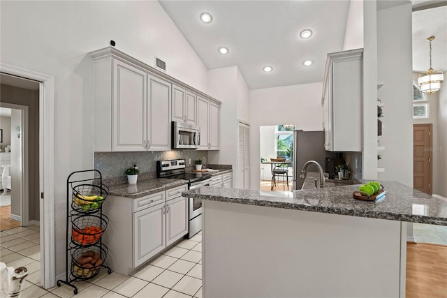 kitchen featuring visible vents, a peninsula, a sink, decorative backsplash, and appliances with stainless steel finishes