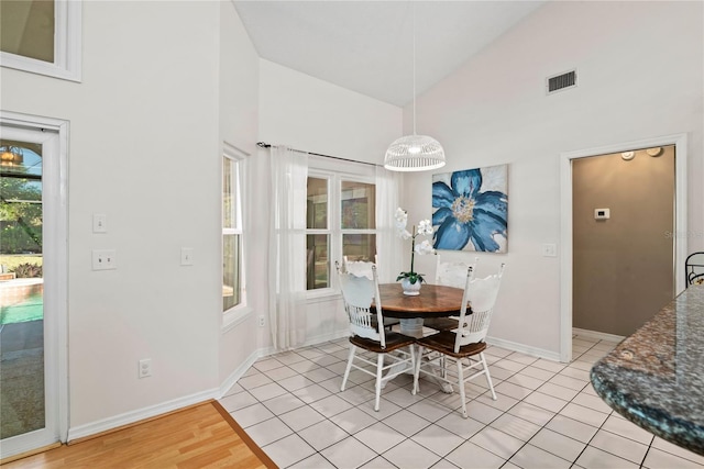 dining space with light tile patterned flooring, baseboards, visible vents, and high vaulted ceiling