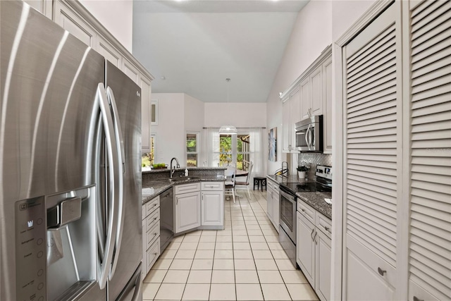 kitchen with a sink, appliances with stainless steel finishes, a peninsula, light tile patterned floors, and decorative backsplash