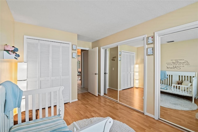 bedroom with two closets, baseboards, and light wood finished floors