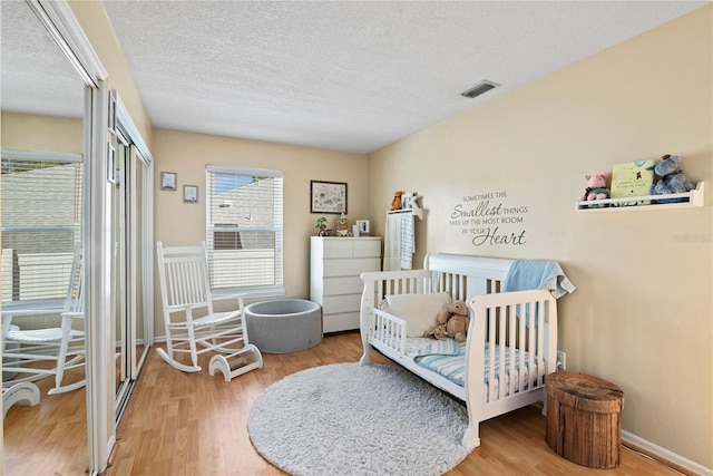 bedroom featuring wood finished floors, baseboards, visible vents, a closet, and a textured ceiling