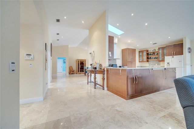 kitchen with high vaulted ceiling, a peninsula, a breakfast bar, brown cabinetry, and glass insert cabinets