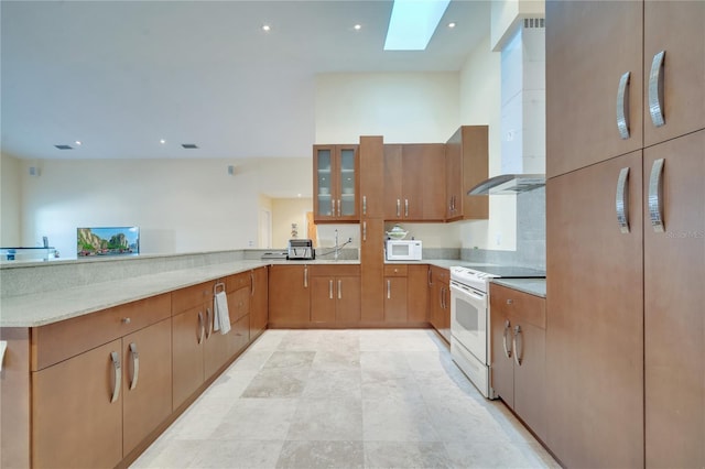 kitchen featuring white appliances, a skylight, wall chimney exhaust hood, glass insert cabinets, and a peninsula