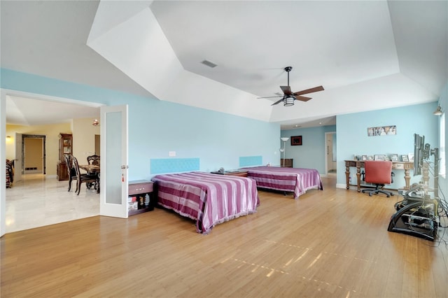 bedroom featuring a tray ceiling, light wood-type flooring, visible vents, and a ceiling fan