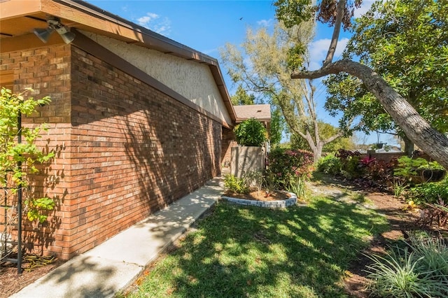 view of side of home with stucco siding, a lawn, and brick siding