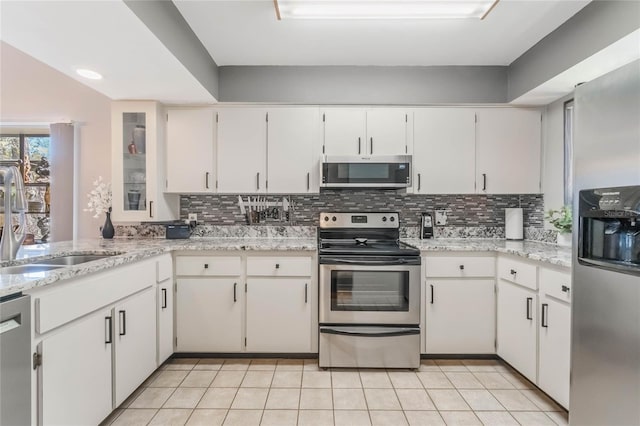 kitchen featuring light tile patterned floors, stainless steel appliances, a sink, white cabinets, and backsplash