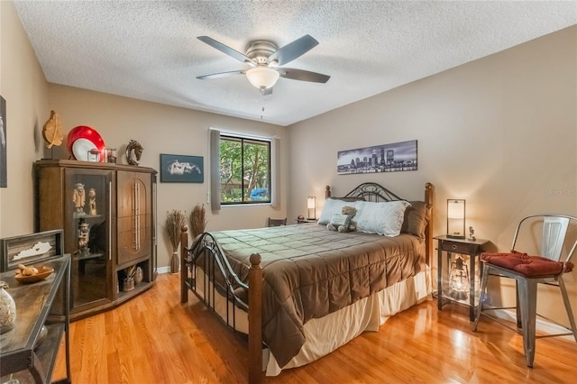 bedroom with a textured ceiling, baseboards, light wood-style flooring, and a ceiling fan