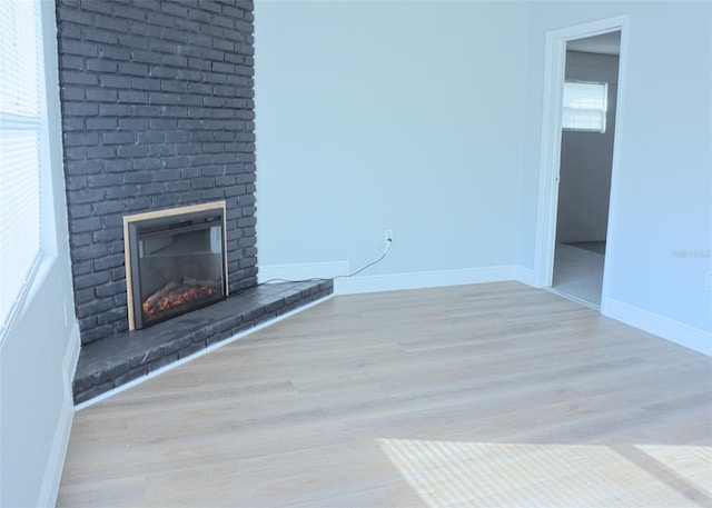 unfurnished living room with a brick fireplace, baseboards, and wood finished floors