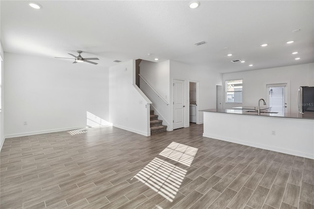 unfurnished living room with visible vents, wood tiled floor, a sink, recessed lighting, and stairs