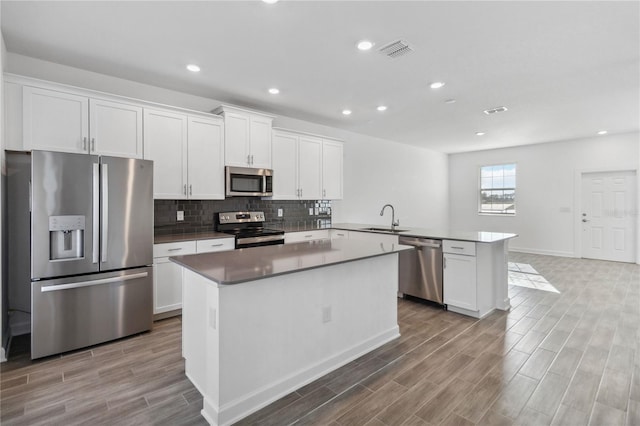 kitchen with visible vents, a sink, stainless steel appliances, a peninsula, and white cabinets