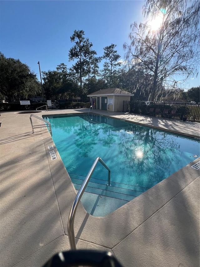 community pool with a patio area, an outbuilding, and fence