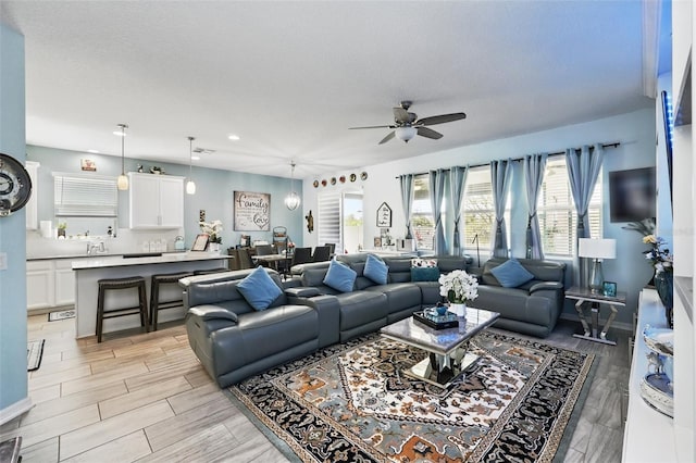 living area featuring baseboards, ceiling fan, light wood-type flooring, recessed lighting, and a textured ceiling