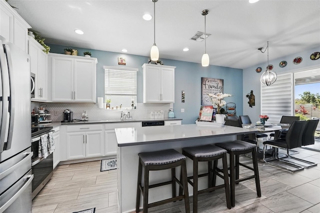 kitchen with visible vents, backsplash, white cabinetry, stainless steel appliances, and a breakfast bar area