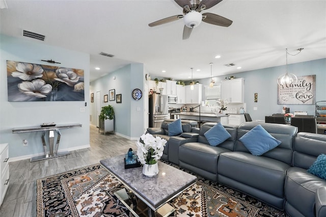 living room with visible vents, ceiling fan with notable chandelier, and baseboards