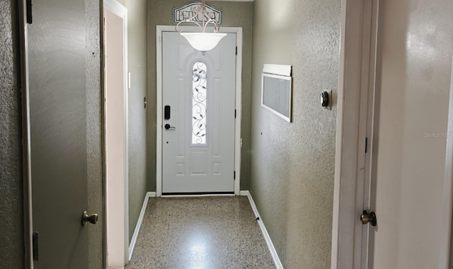 doorway to outside featuring a textured wall, speckled floor, and baseboards