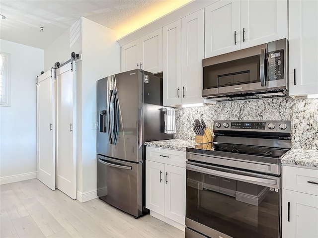 kitchen with a barn door, light stone countertops, appliances with stainless steel finishes, and decorative backsplash